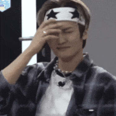 a man wearing a headband with stars on it is covering his eyes