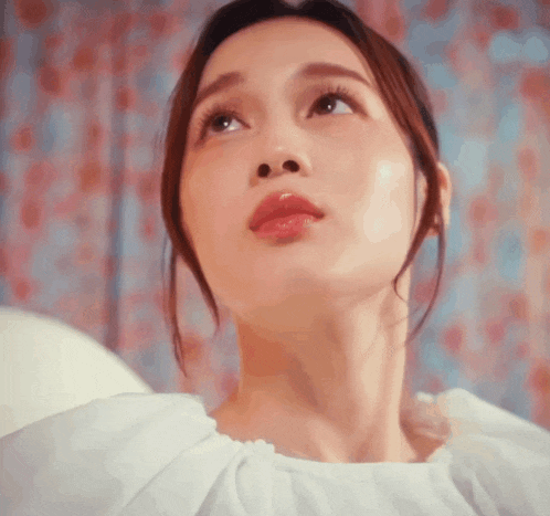 a close up of a woman 's face with a white shirt on looking up at the sky .