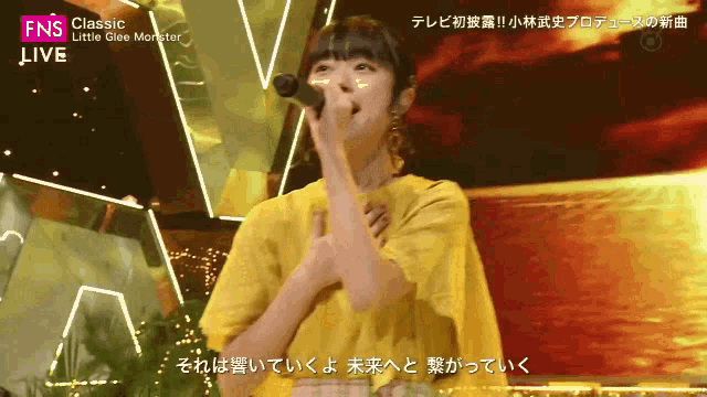 a woman in a yellow shirt singing into a microphone with the words classic little glee monster on the bottom right