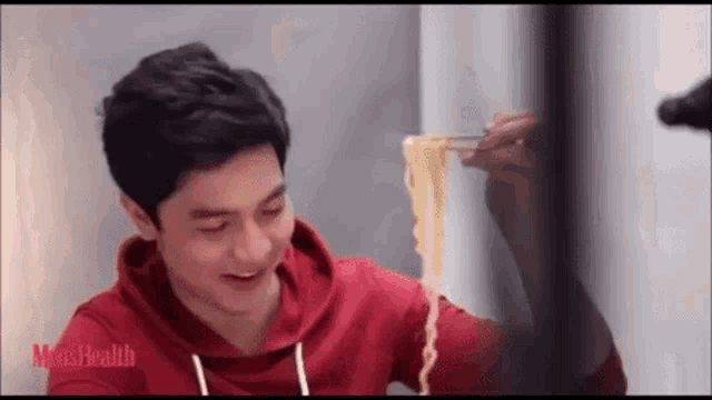 a man is eating noodles with chopsticks and smiling .