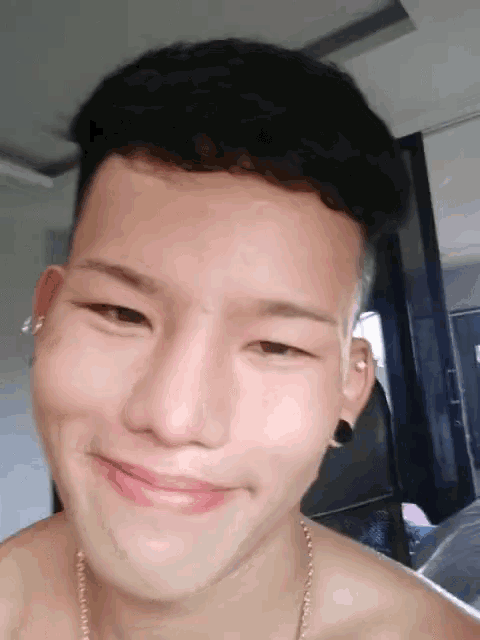 a shirtless man with a necklace around his neck smiles