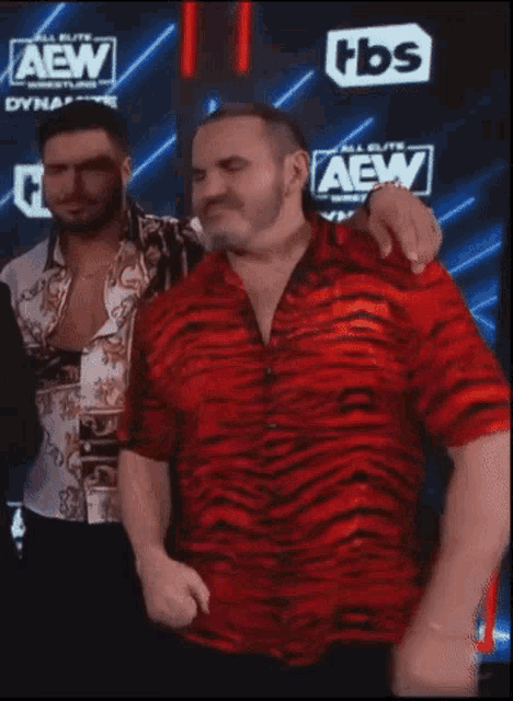 a man in a tiger print shirt is standing in front of a wall that says aew on it