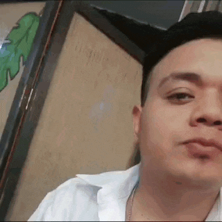 a man in a white shirt is looking at the camera while standing in front of a door .