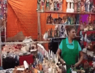 a woman in a green apron stands in front of a display of figurines