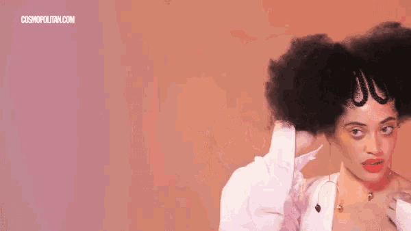 a woman with a big afro is wearing a white shirt and earrings and has her eyes closed .