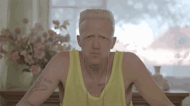a man wearing a yellow tank top has a tattoo on his arm that says ' i 'm a boy '