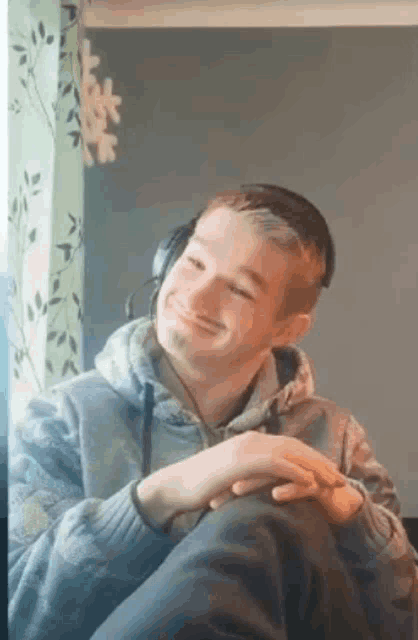 a young man wearing headphones is sitting on a couch in front of a window .