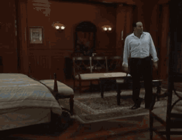 a man in a white shirt and black pants stands in front of a bed