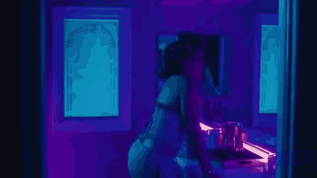 a woman is standing in front of a mirror in a dark room with purple lights .