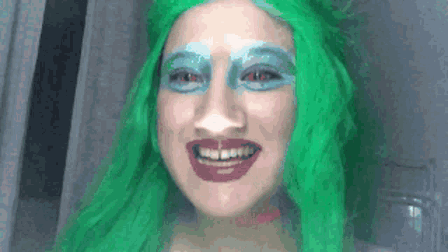 a woman with green hair and blue eyeshadow is smiling .