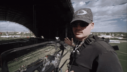 a man wearing sunglasses and an oakley hat stands in front of a stadium