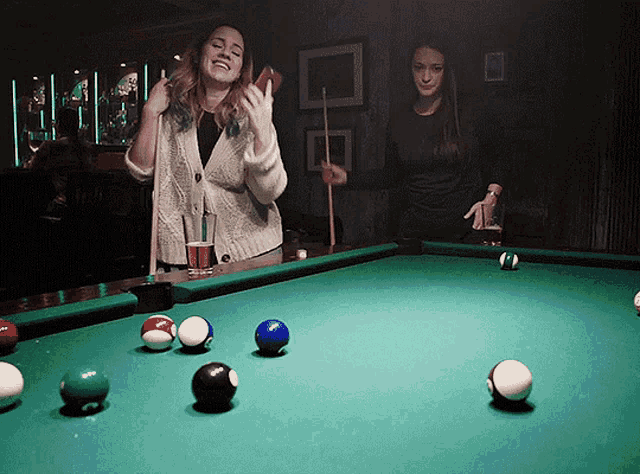 two women are playing pool together and one is holding a cue stick