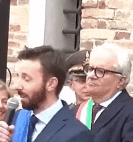a man in a suit and tie is speaking into a microphone while standing next to another man .