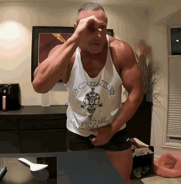 a man wearing a gold 's gym tank top holds his hand to his forehead