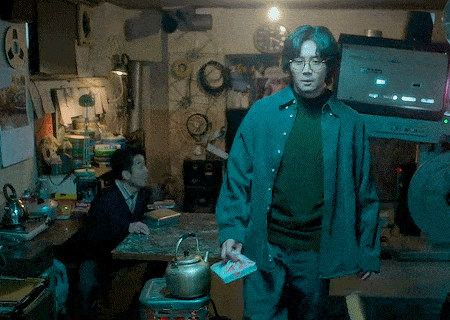 a man in a green shirt is standing in a room with a clock on the wall above him