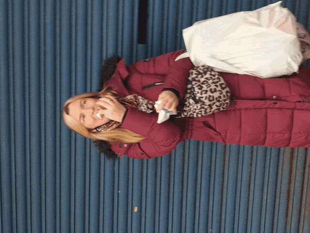 a woman in a burgundy coat is eating a sandwich