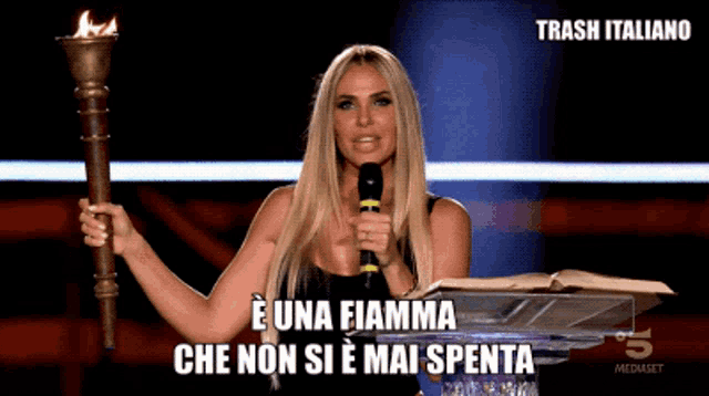 a woman is holding a torch and speaking into a microphone with trash italiano in the corner