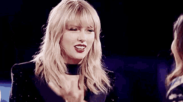 taylor swift is applauding while standing next to a woman on stage .