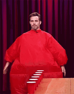 a man in a red suit is standing in front of a row of red cups on a table
