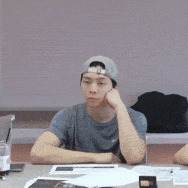 a man wearing a baseball cap is sitting at a table with a cup of coffee in front of him