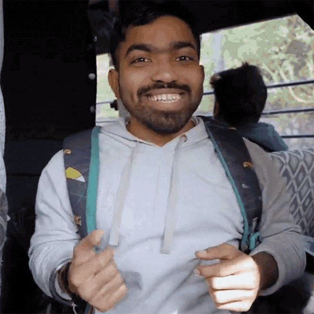 a man with a beard wearing a white hoodie and a blue backpack