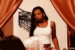 a woman in a white tank top is standing in front of a window .