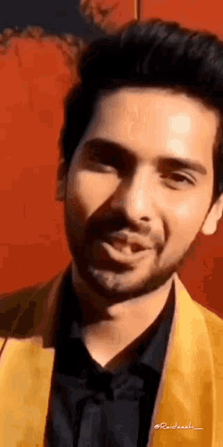a man with a beard is wearing a yellow jacket and a black shirt and smiling .