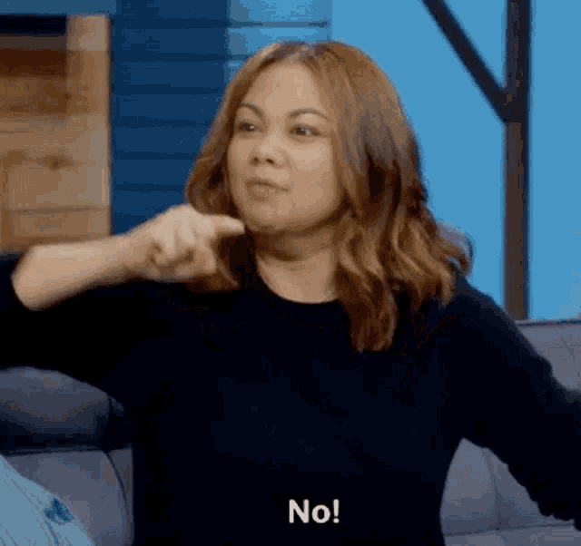 a woman is sitting on a couch and pointing at the camera while saying no .