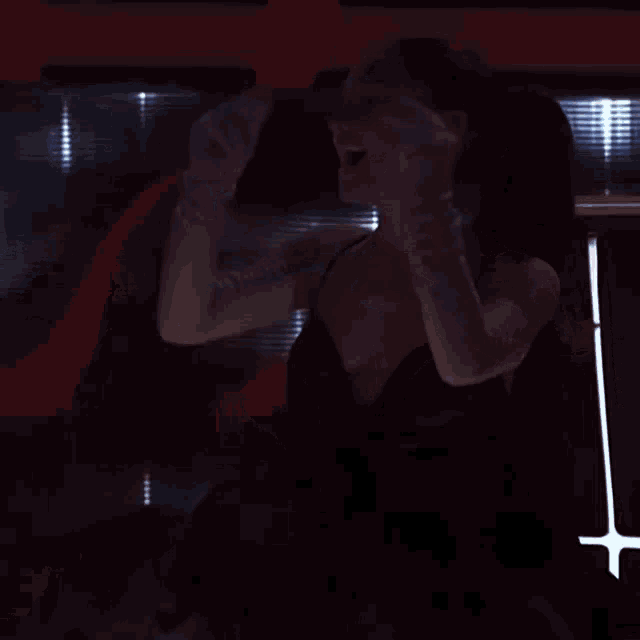 a woman in a black dress and white gloves is dancing in a dark room