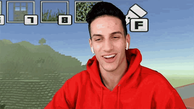 a man wearing a red hoodie is smiling in front of a pixelated background with the letter f on it
