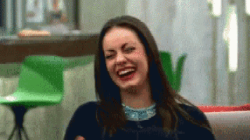 a woman is sitting on a couch laughing with her eyes closed .