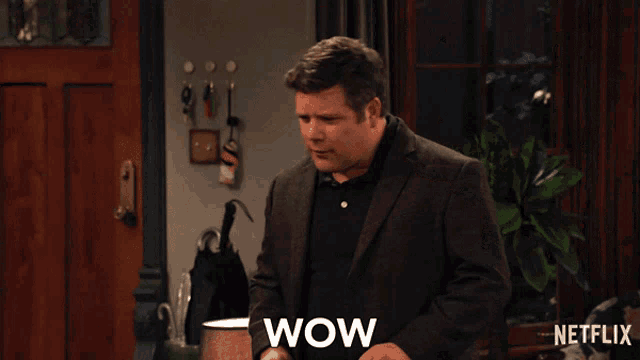 a man in a suit sits on a couch with a woman and says wow on the bottom