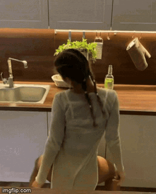 a woman in a white shirt is standing in front of a sink in a kitchen