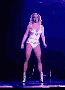 a woman in a white bodysuit is dancing on a stage in front of a microphone .