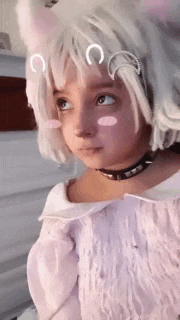 a little girl wearing a white wig and a choker is looking up .