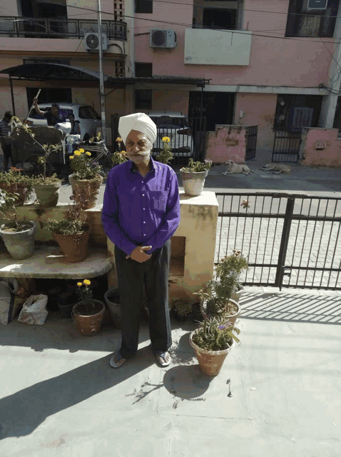 a man wearing a turban and a purple shirt is standing in front of potted plants