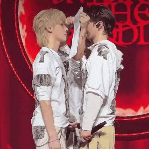 a man wipes another man 's face with a towel in front of a sign that says " the idol "