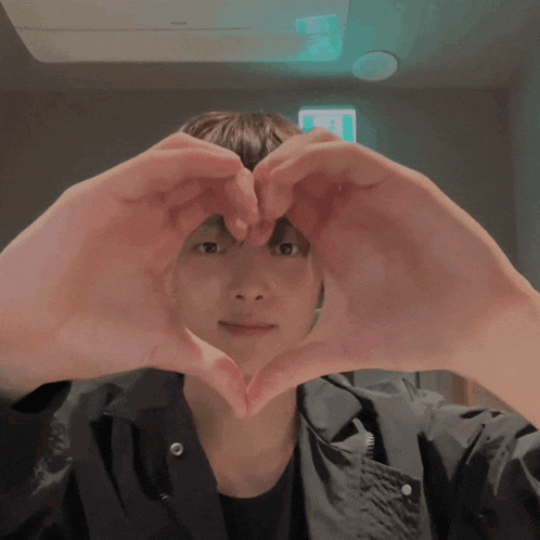 a man making a heart shape with his hands in front of his face