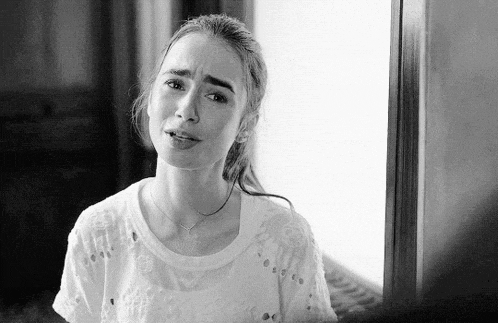 a black and white photo of a woman standing in front of a window with her eyes closed .