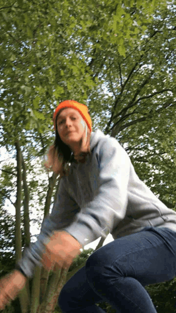 a woman wearing an orange beanie and a grey hoodie is squatting down