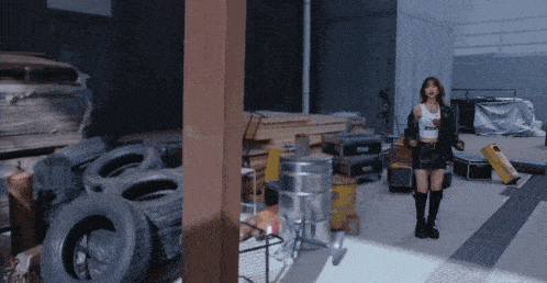a woman in a crop top stands in a warehouse surrounded by tires and other items
