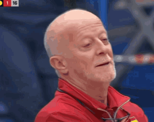 a bald man wearing a red jacket and glasses with the number 16 in the corner