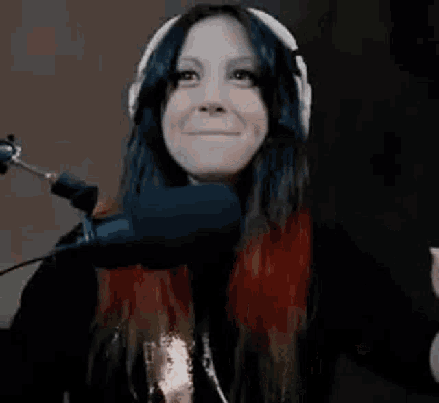 a woman wearing headphones is standing in front of a microphone and making a funny face .