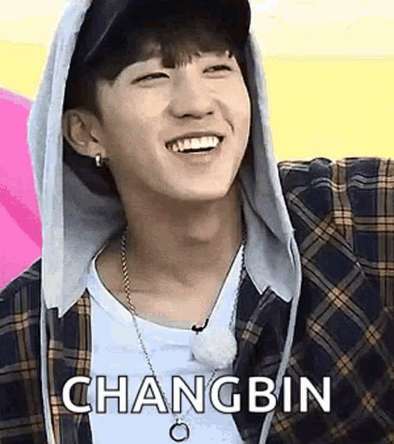 a young man wearing a plaid shirt and a hoodie is smiling and wearing a necklace .