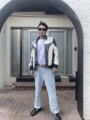 a man wearing sunglasses and a leather jacket is standing in front of a white building
