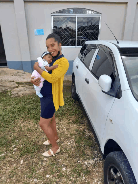 a woman holding a baby in front of a car