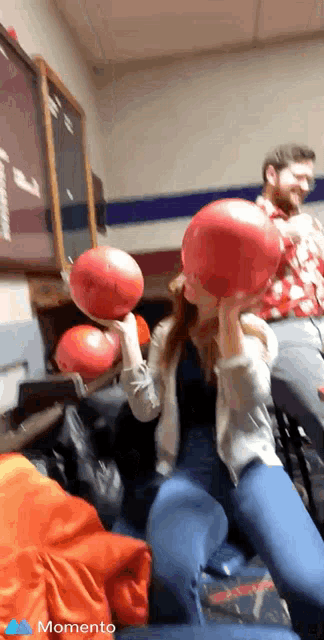 a woman is holding a bowling ball over her head while a man watches