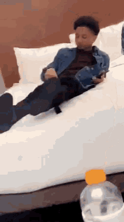 a young man is laying on a bed with his feet up and a bottle of water next to him .