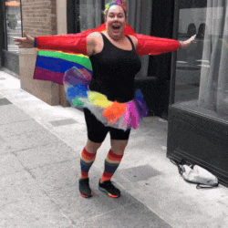 a woman wearing a rainbow skirt and socks is standing on the sidewalk with her arms outstretched