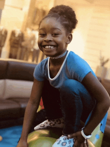 a little girl in a blue shirt is kneeling on a green ball